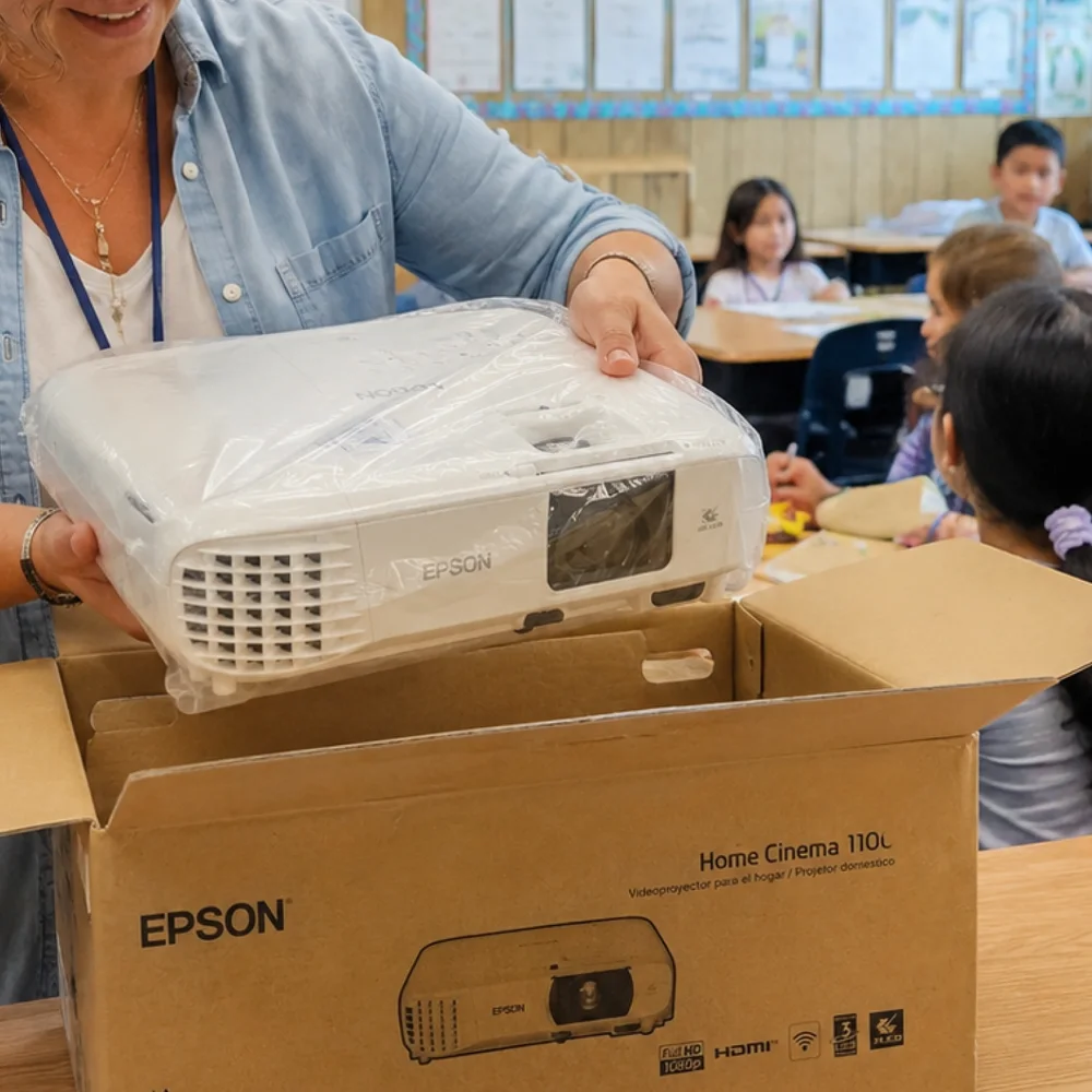 Teacher unpacking classroom equipment while students sit nearby