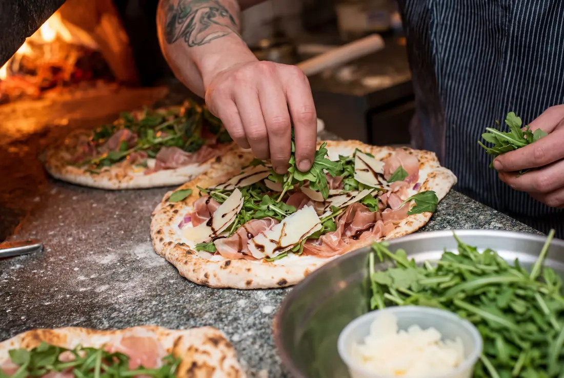 Restaurant cook topping a fresh pizza